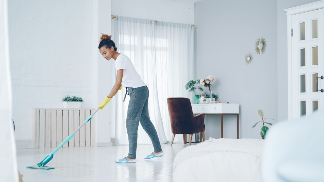 team-01 Jeune femme afro-américaine nettoyant le sol chez elle avec une serpillière plate en plastique, gantée et vêtue de vêtements d’intérieur. Intérieurs modernes, propreté et jeunesse au cœur du concept.